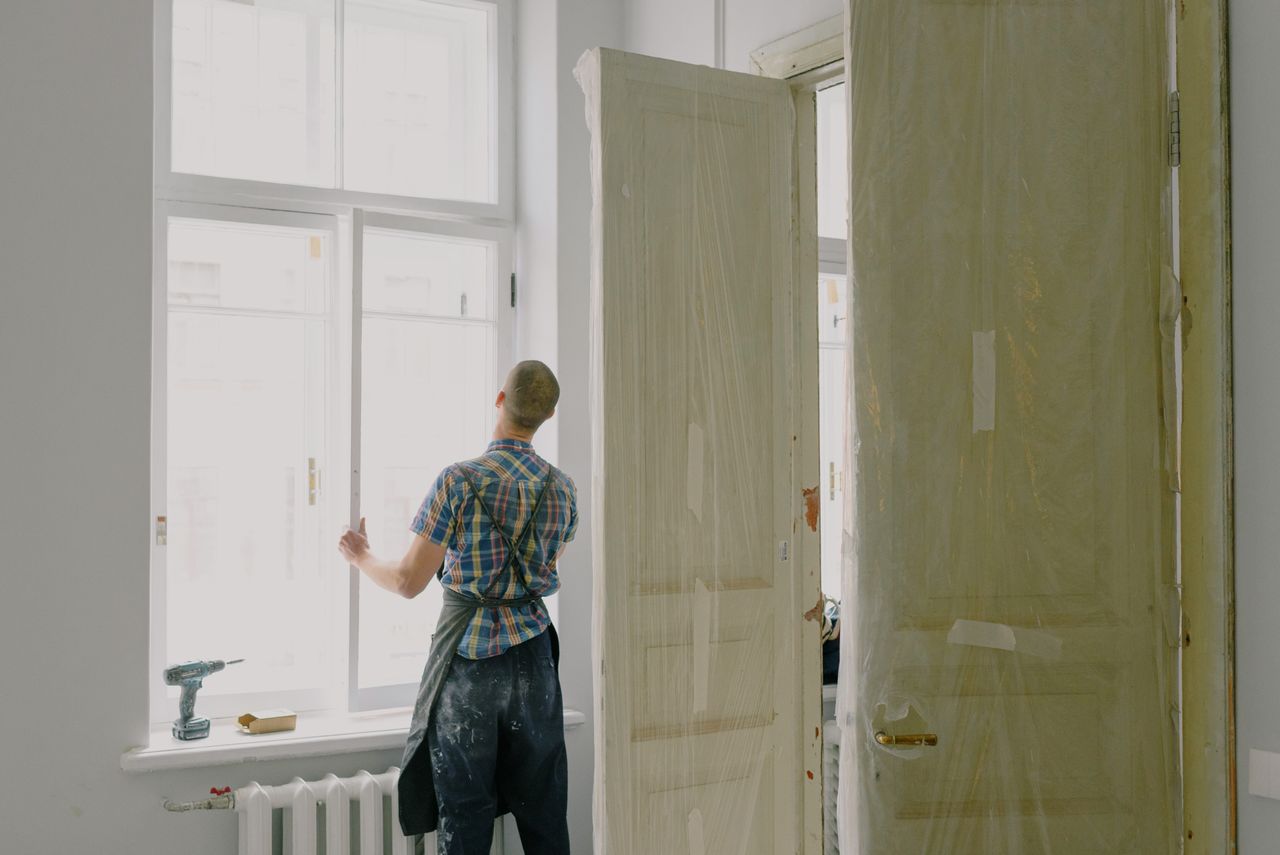 Réalisations Back view of unrecognizable workman in apron mounting window near drilling machine and doors in flat